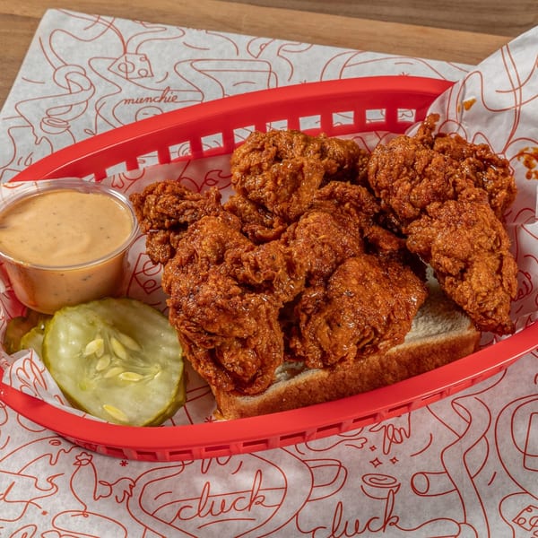 Cluck Kitchen's fried chicken tenders in a red basket with pickles and dipping sauce.