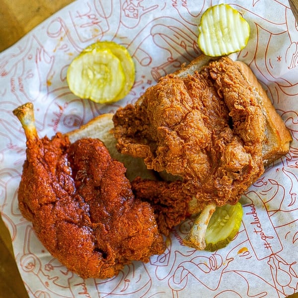 Cluck Kitchen's fried chicken sandwich with a spicy chicken leg and pickles on branded paper.