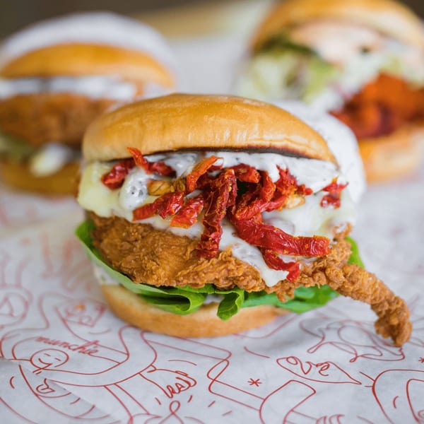 Cluck Kitchen fried chicken sandwich with melted cheese, sun-dried tomatoes, and lettuce on a bun.