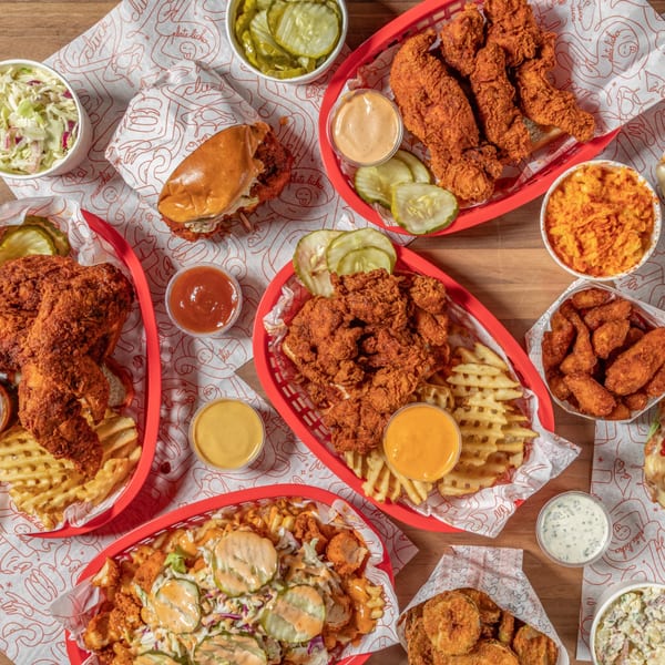 An overhead shot of various fried chicken dishes, fries, sides, and sauces from Cluck Kitchen.