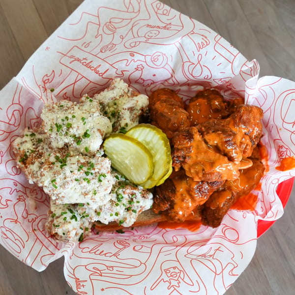 Cluck Kitchen's fried chicken wings, half with white sauce and chives, half with orange sauce, and pickles.