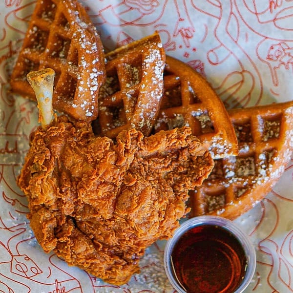 Cluck Kitchen's fried chicken and waffles, dusted with powdered sugar, with a side of syrup.