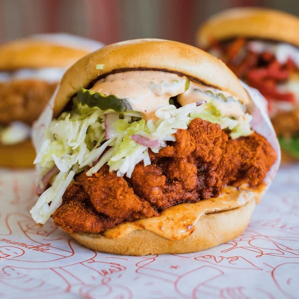 Cluck Kitchen's fried chicken sandwich with coleslaw, pickles, and sauce on a bun.