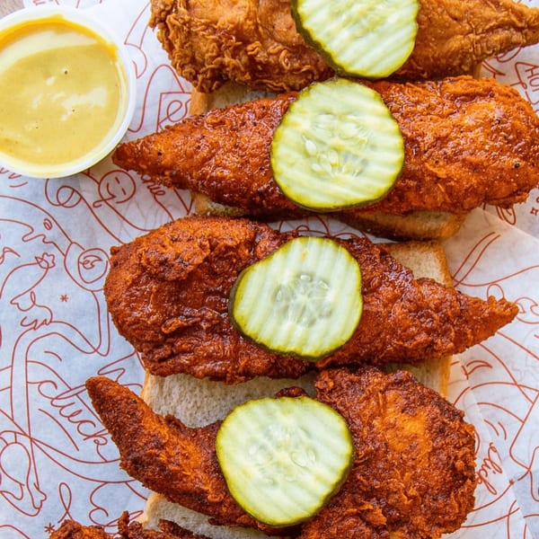 Cluck Kitchen's fried chicken tenders with pickles on white bread, served with a side of sauce.