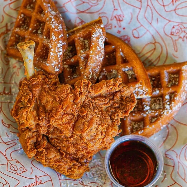 Cluck Kitchen's fried chicken and waffles, dusted with powdered sugar, served with a side of syrup.