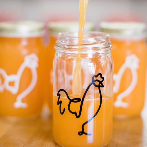 Orange juice being poured into a Cluck Kitchen mason jar with a chicken logo.