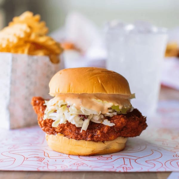Cluck Kitchen's fried chicken sandwich with coleslaw and sauce, with fries and a drink in the background.